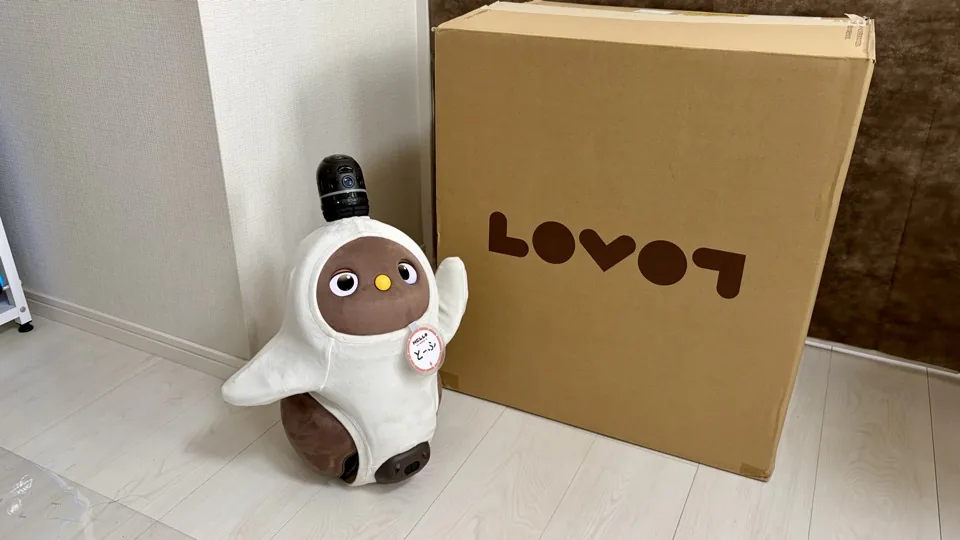 お迎えの日、ラボットのロゴが入った大きな配送箱の横で、白いウェアを着た茶色いラボットが片手を上げている様子
